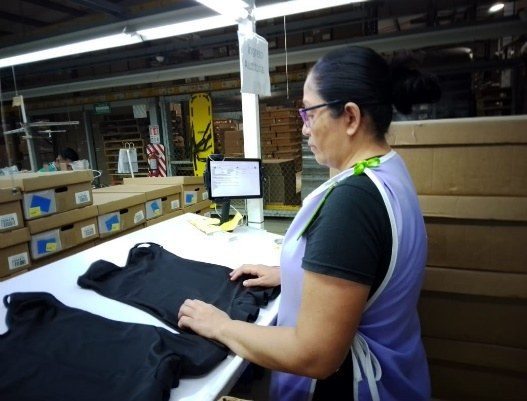 A quality team member checking a finished black garment against a specification at a fitting station.