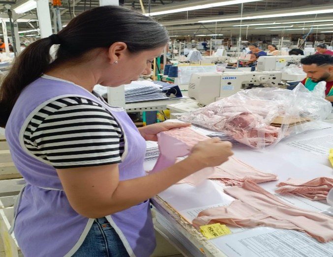A quality team member inspecting finished pink garments at an audit table.