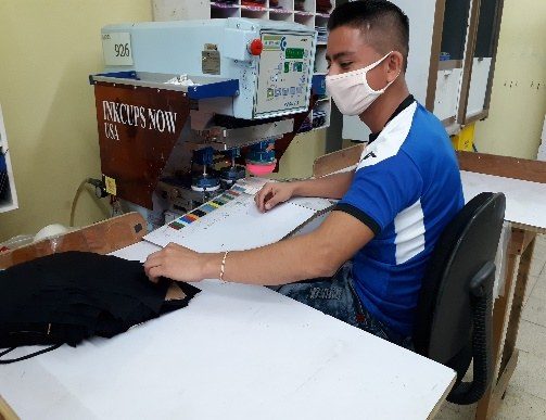An operator running a pad printing machine on dark garment panels.