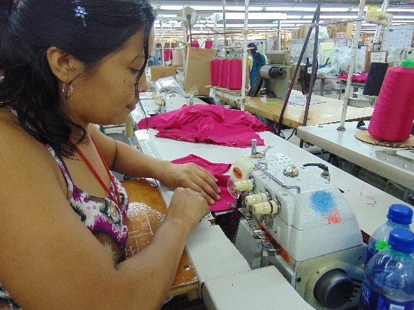 An operator sewing a bright pink knit garment at an overlock machine.