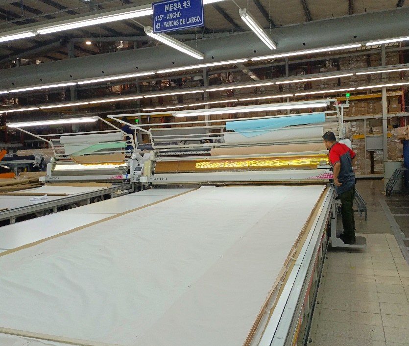 A long automated spreading table with rolls of fabric staged above it.